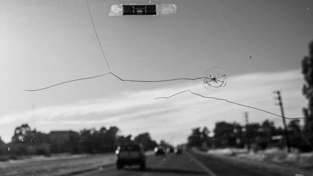 A crack spreading across a car windshield with the road ahead visible through the glass